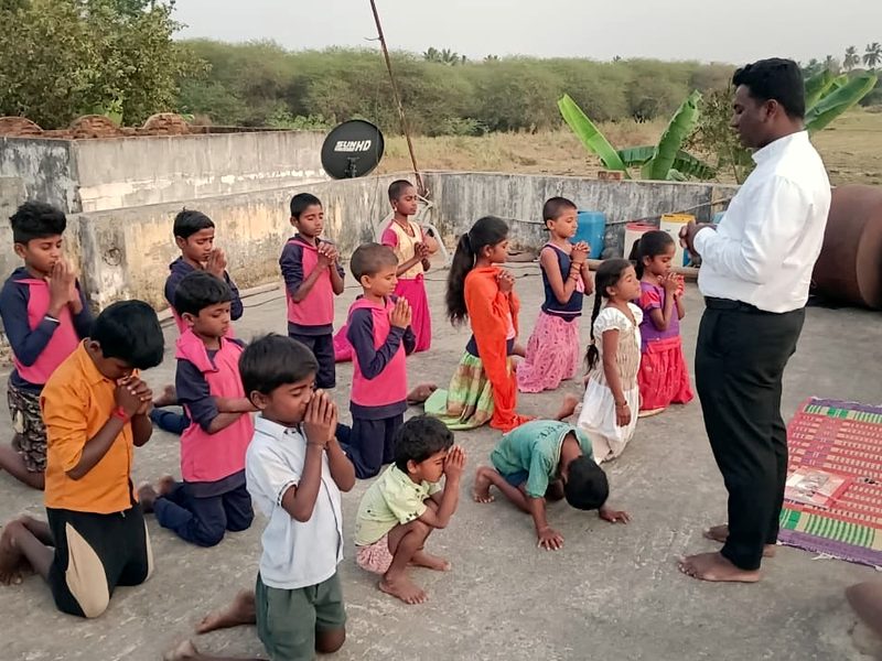 Village children kneeling in prayer with a pastor on a rooftop near Cheyyar, India